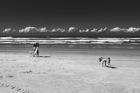 Serene black and white beach scene with a solitary figure and dog at Praia Grande, Brazil.