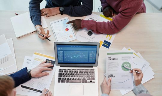 Top view of colleagues analyzing data on a digital device in an office setting.