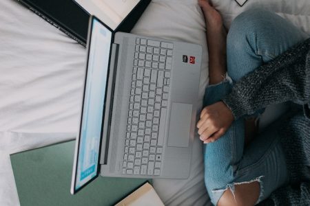 woman in blue long sleeve shirt and blue denim jeans sitting on bed using laptop